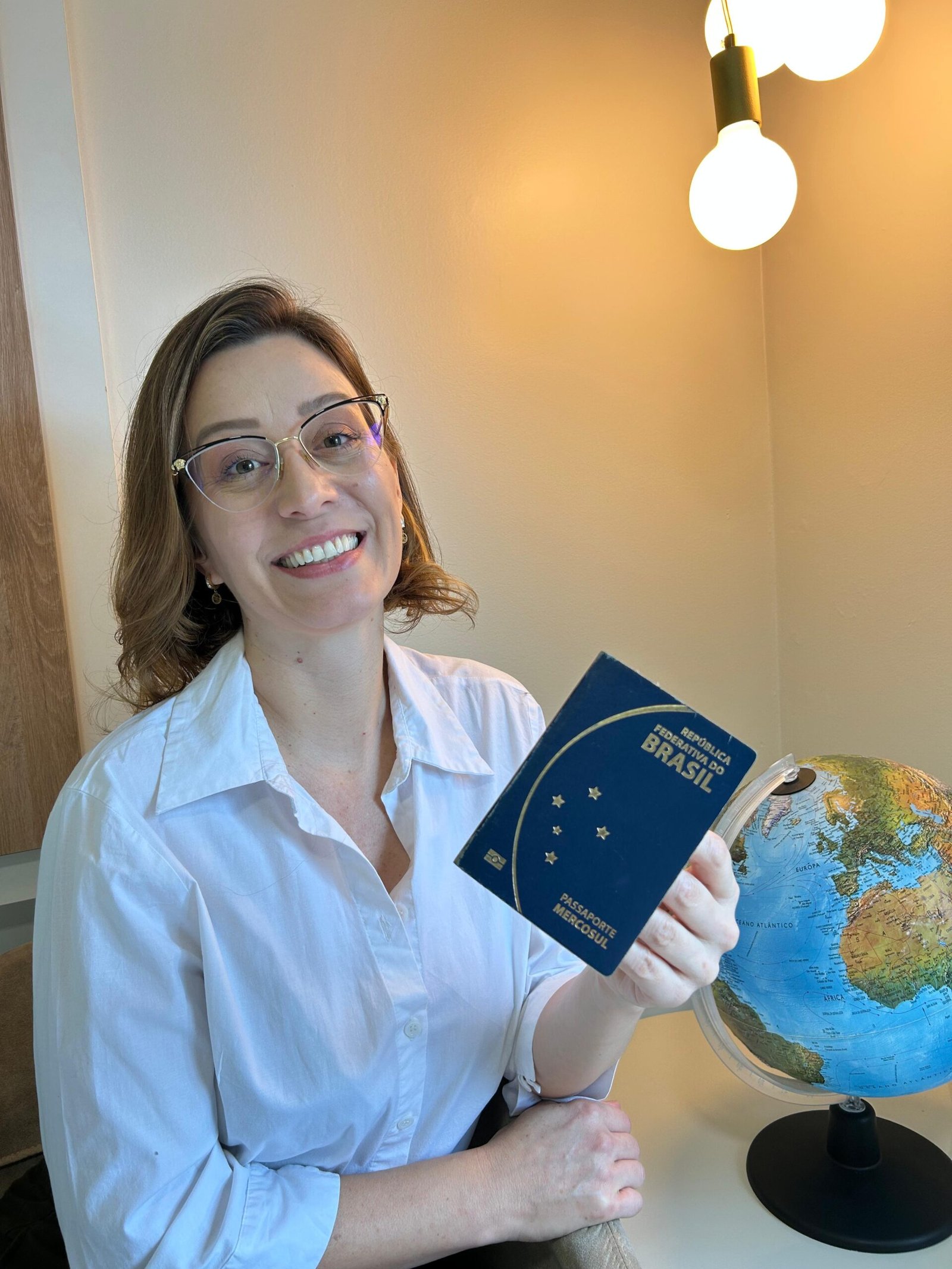 Giseli segurando o passaporte brasileiro ao lado de um globo